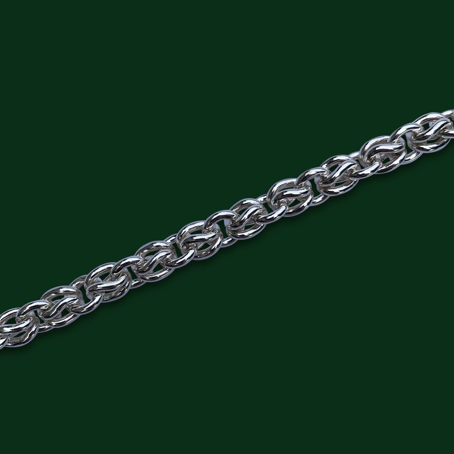 A close up of Timio's Anniversary chain on a dark green background, emphasizing the closely curved links.