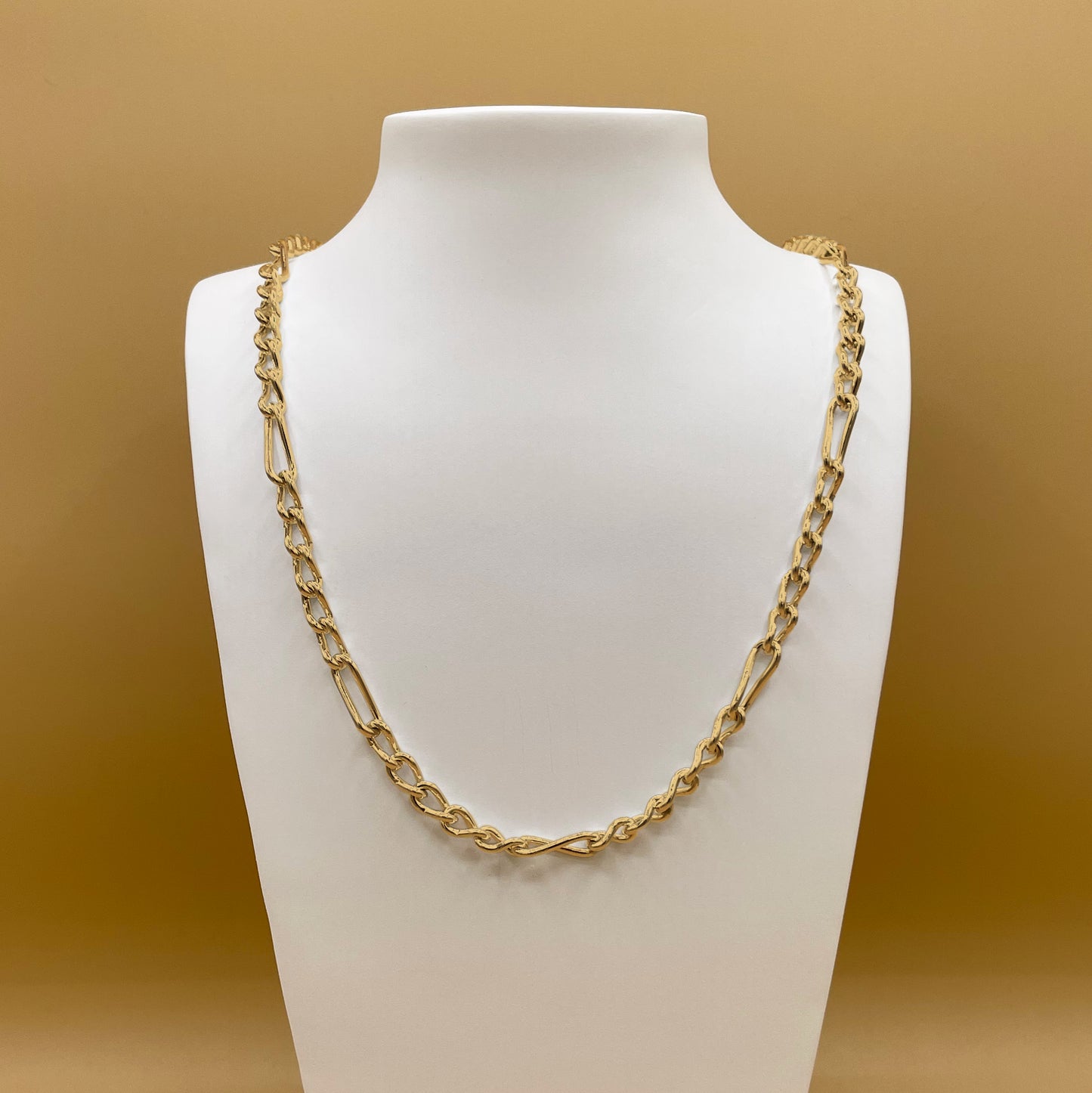 Timio's Armoni chain, in 24 karat gold, displayed on a white bust in front of a golden background.