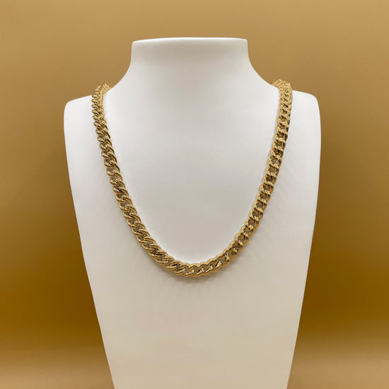 Timio's Curb chain, in 24 karat gold, displayed on a white bust in front of a golden background.