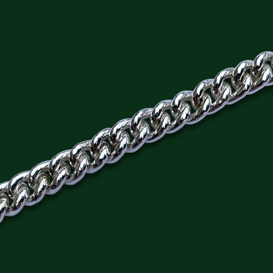 A close up of Timio's Curb chain, in medium weight, on a dark green background.