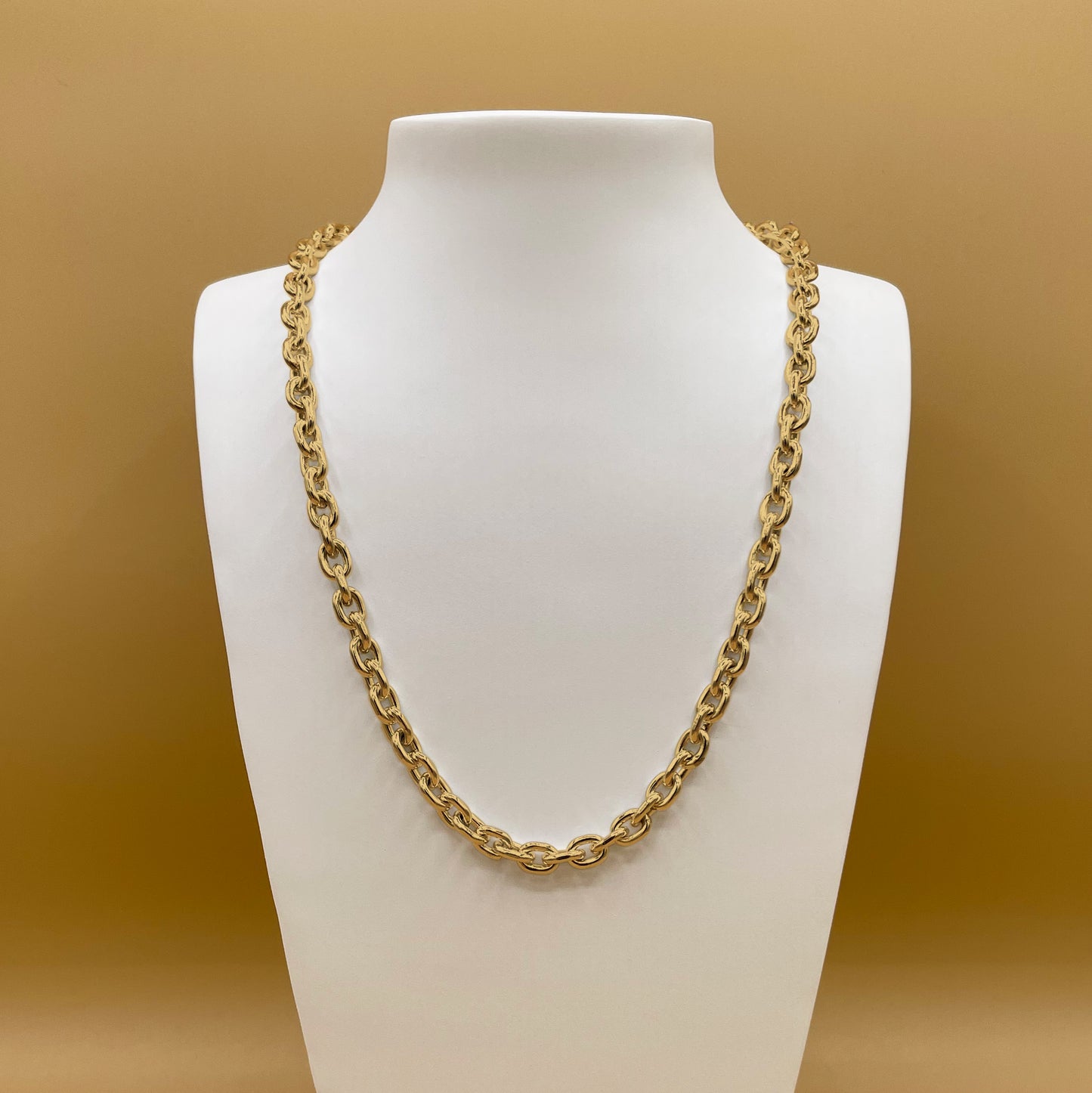 Timio's Desmo chain, in 24 karat gold, displayed on a white bust in front of a golden background.