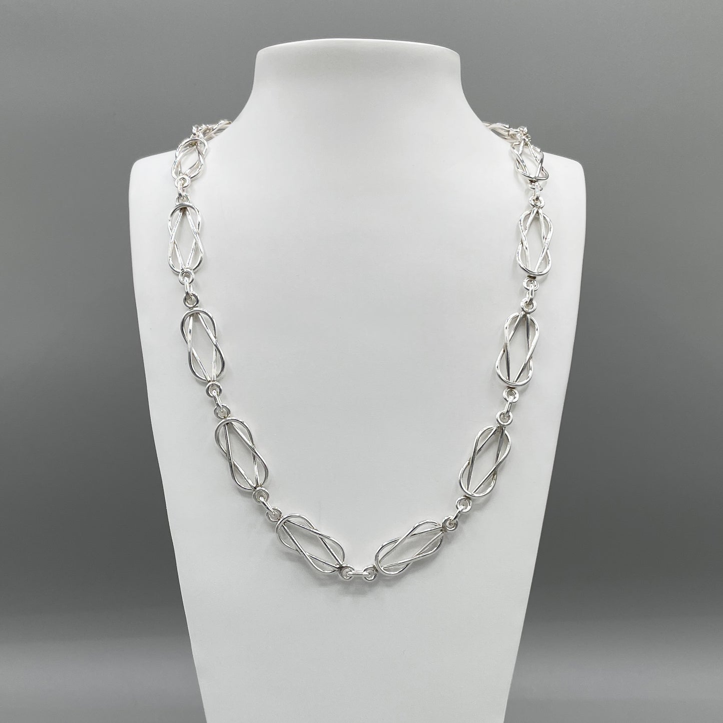 A photo of the Forget-Me-Knot chain displayed on a white bust in front of a grey background.