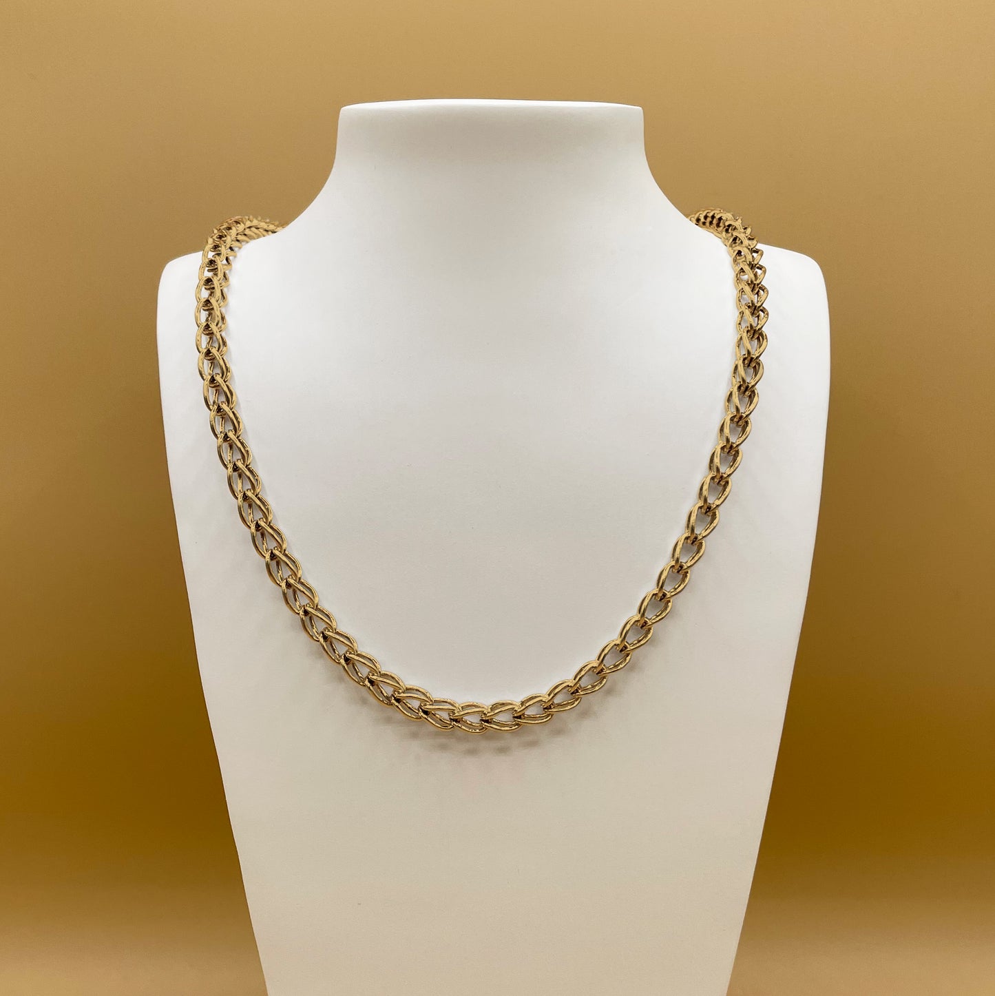 A photo of Timio's Kubos chain in 24 karat gold, displayed on a white bust in front of a golden background.