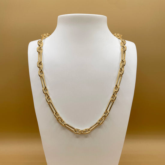 The Makarios style chain in 24 karat gold on a white bust stand in front of a light, golden background.