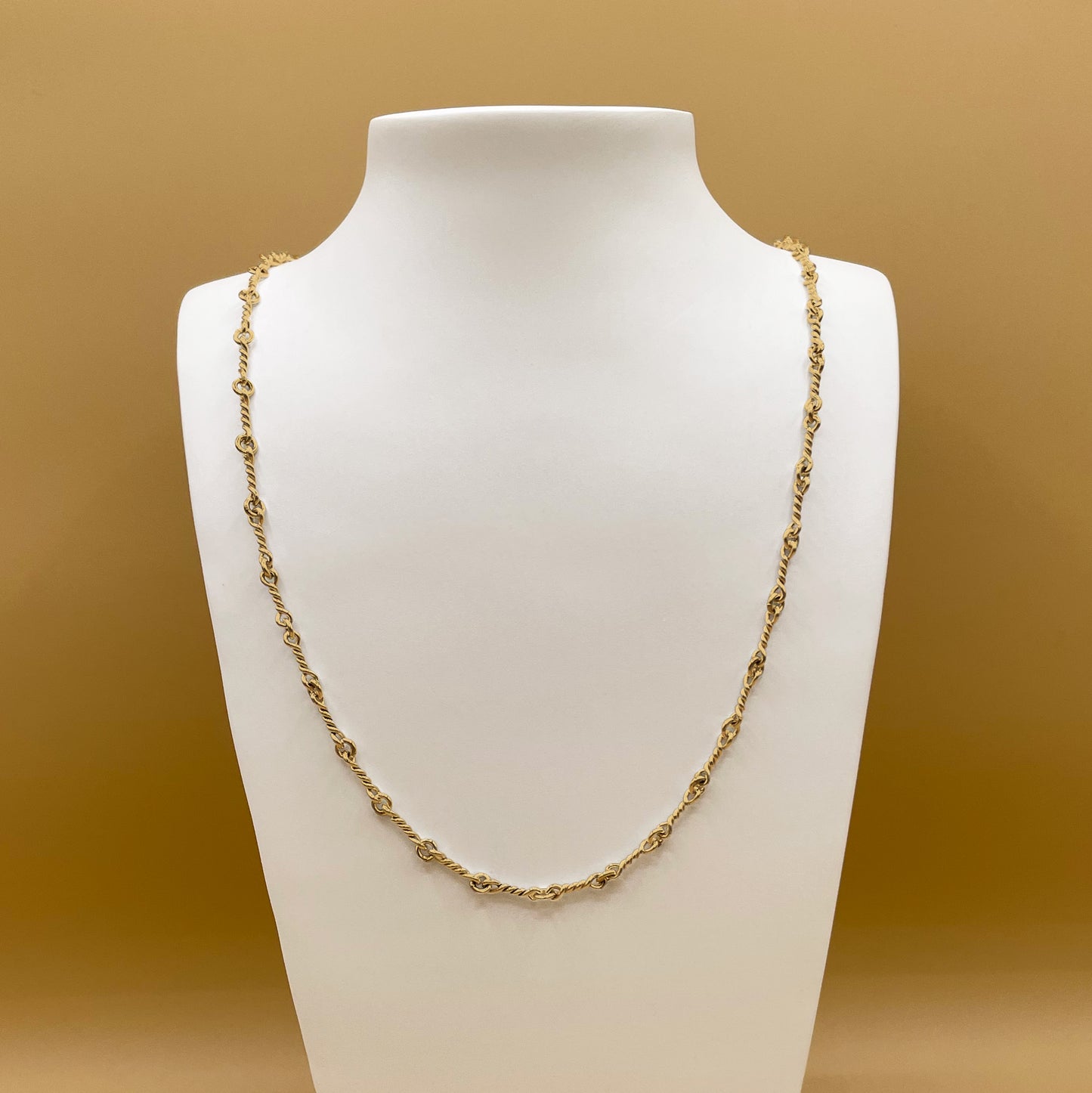 Timio's Nautical chain, in 24 karat gold, displayed on a white bust in front of a golden background.