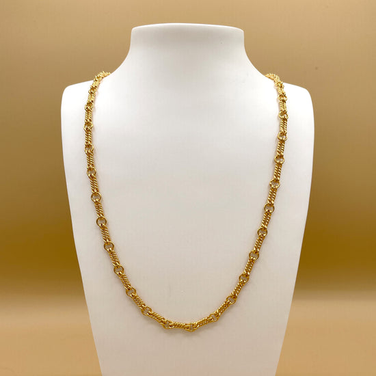 The Double Nautical chain in 24 karat gold displayed on a white bust in front of a light, golden background.