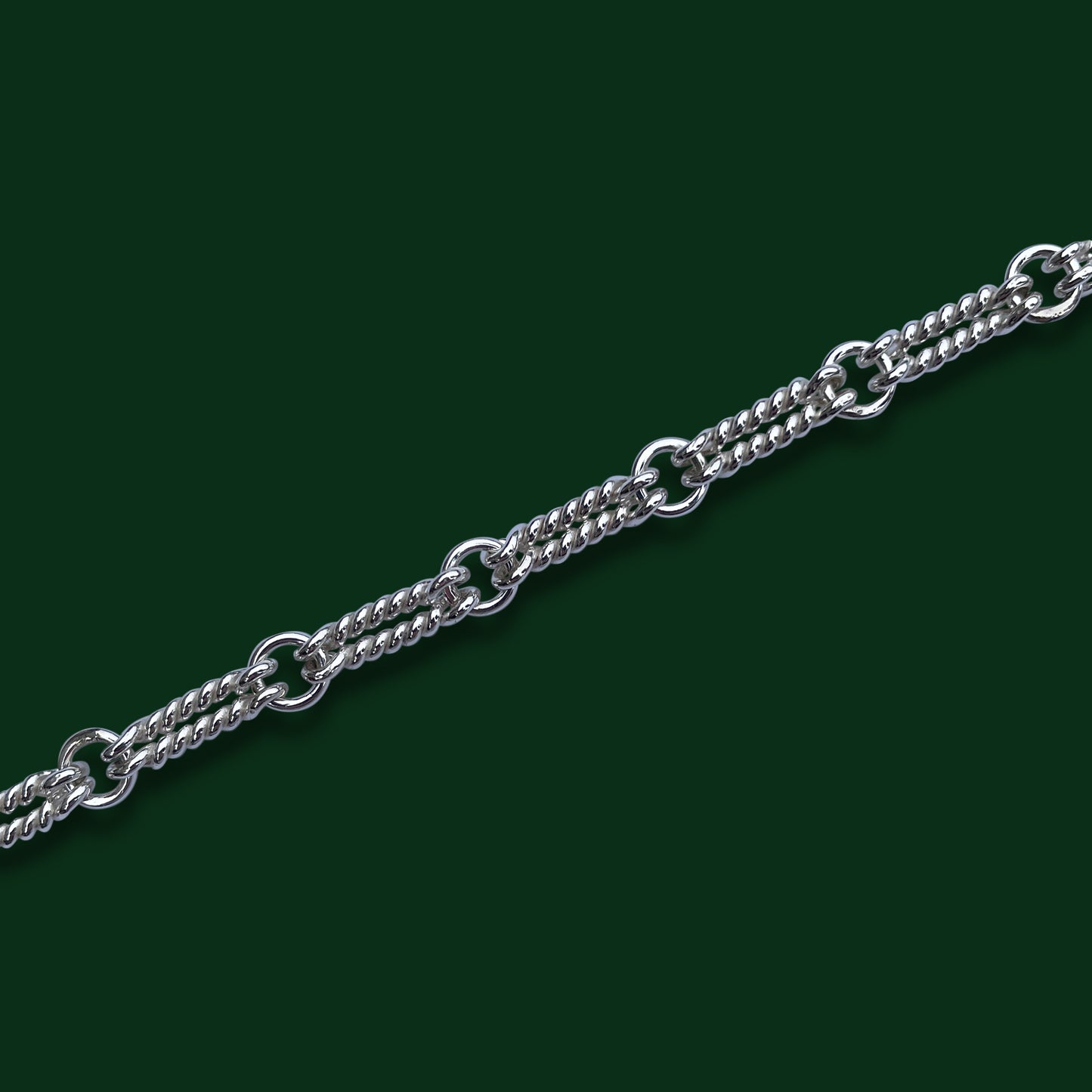 A close up of TImio's Double Nautical chain on a dark green background, emphasizing the pairs of long twisted links joined by small circle links.