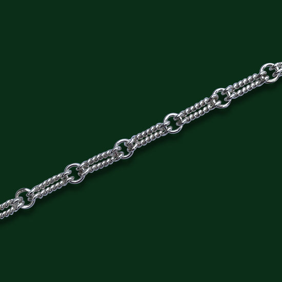 A close up of TImio's Double Nautical chain on a dark green background, emphasizing the pairs of long twisted links joined by small circle links.