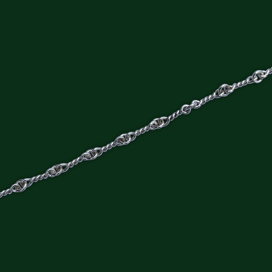 A close up view, on a dark green background, of Timio's Nautical chain which features twisted links joined by circle links.