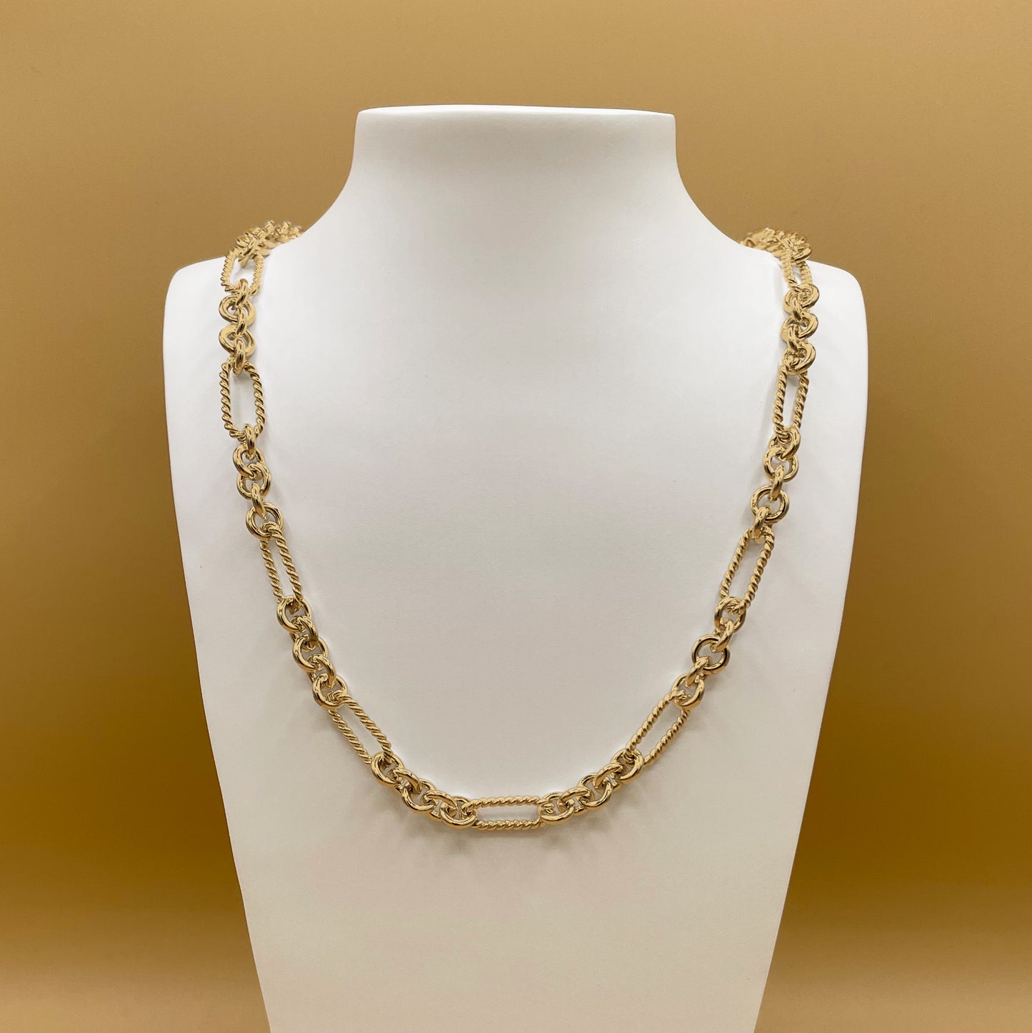 A photo of Timio's Soiree chain in 24 karat gold displayed on a white bust in front of a golden background.