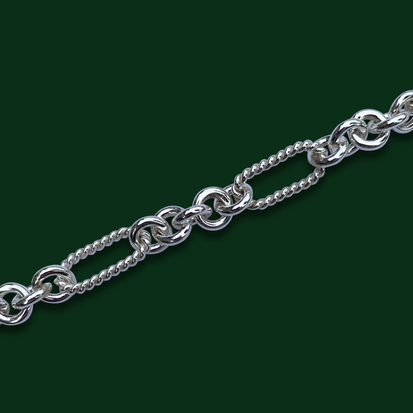 A close up of Timio's Soiree style on a dark green background, emphasizing its five small circles to every twisted, long oval link.